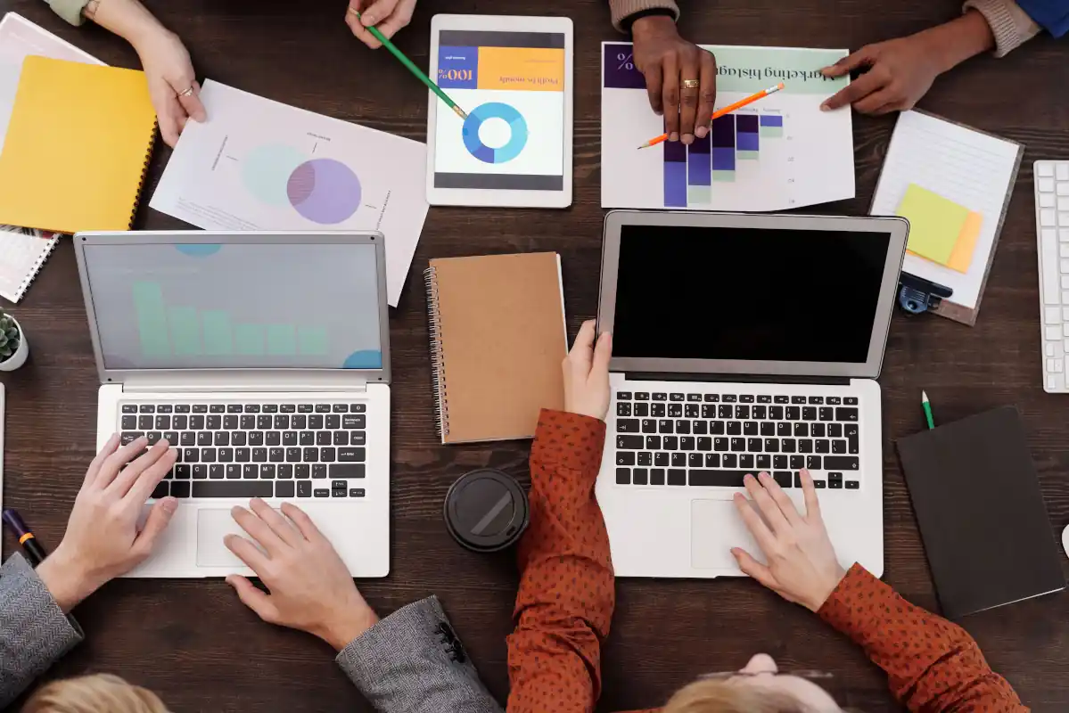 A meeting table with two laptops, notebooks, printed reports and coffee